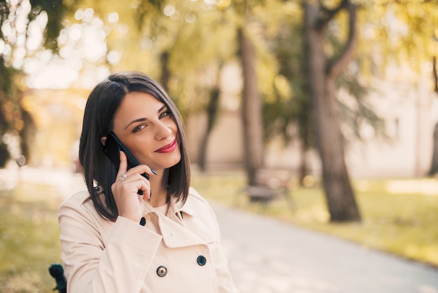 Young beautiful smiling woman talking on cell phone in park.