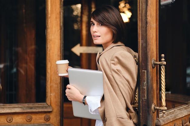 Young beautiful stylish businesswoman with laptop and coffee going on work outdoor