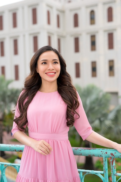 Young beautiful stylish girl in pink dress walking and posing between city