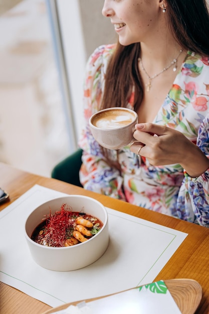 Young beautiful stylish woman drinking coffee while sitting in restaurant and eating tasty dish