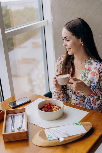 Young beautiful stylish woman drinking coffee while sitting in restaurant and eating tasty dish