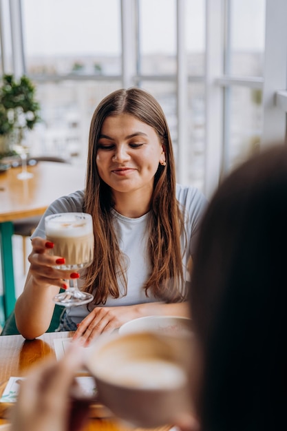 Young beautiful stylish woman drinking coffee while sitting in restaurant during meeting with friend