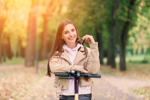 Young beautiful stylish woman riding electric scooter by autumn park ecological transport