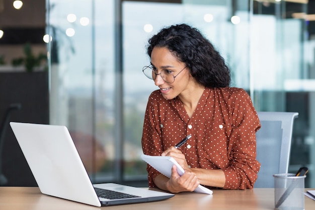 Young beautiful and successful business woman studying remotely sitting in the office hispanic woman