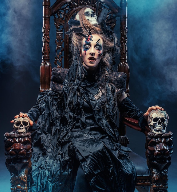 Young beautiful witch sits on a chair Bright make up skull smoke halloween theme