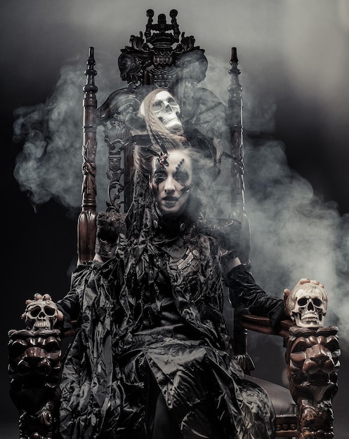 Young beautiful witch sits on a chair Bright make up skull smoke halloween theme