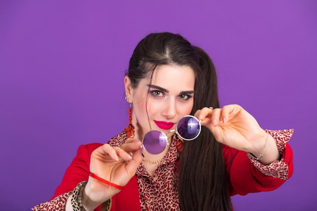 Young beautiful woman in 90s style shows round glasses to the camera