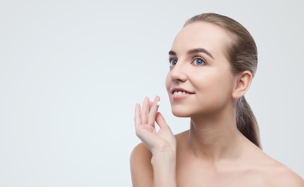 Young beautiful woman applying face cream on grey background