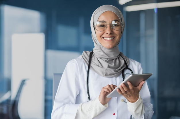 Young beautiful woman asian muslim doctor in hijab smiling and looking at camera working with tablet