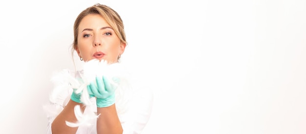 Young beautiful woman beautician in protective green gloves standing and blowing on feathers