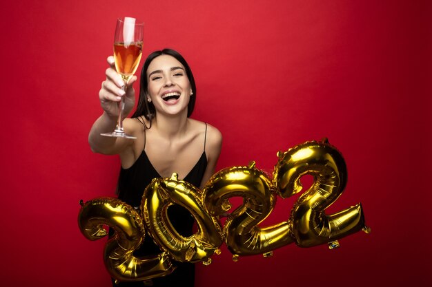 A young beautiful woman in a black dress holds the numbers 2022 and a glass of champagne