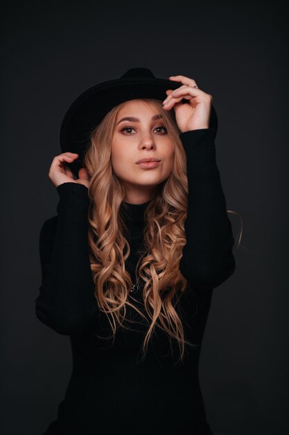 Young beautiful woman in black hat sitting on black wall