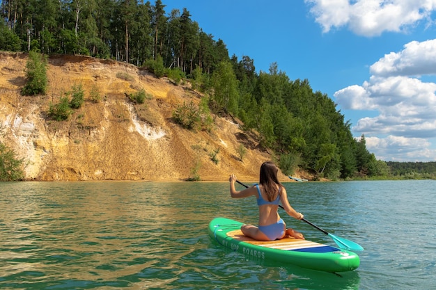 Young beautiful woman in blue bikini is riding on sup board by the Dzerzhinsky quarries.