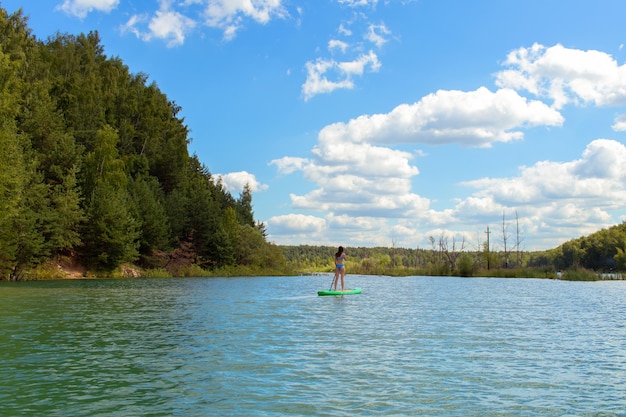 Young beautiful woman in blue bikini is riding on sup board by the Dzerzhinsky quarries.