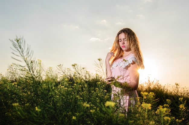 Young beautiful woman in a blue dress enjoying chamomile field among mountains. Summer mood