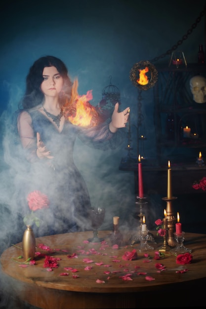 Young beautiful woman in blue vintage dress with red roses and magic potions in dark room