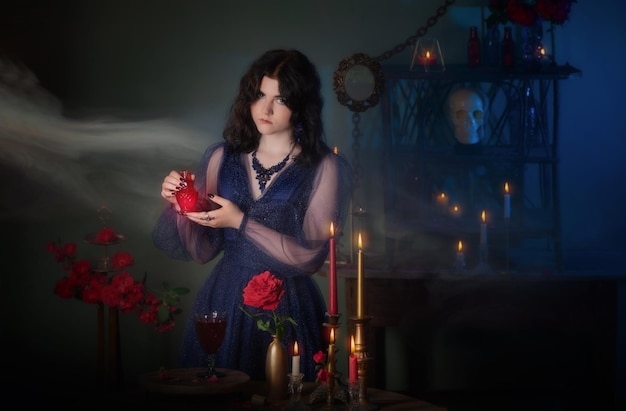 Young beautiful woman in blue vintage dress with red roses makind potion in dark room