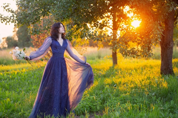 Young beautiful woman in blue vintage dress with white flowers at sunset