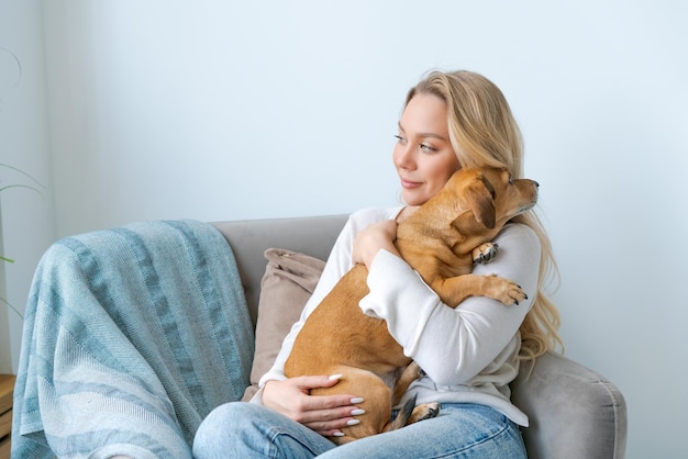 A young beautiful woman in casual clothes hugs and pets her beloved dog sitting