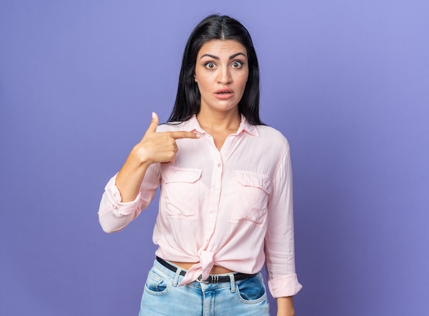 Young beautiful woman in casual clothes surprised pointing at herself standing on blue