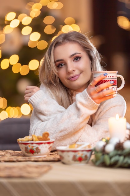 Young beautiful woman in a Christmas atmosphere holding a cup with coffee or tea