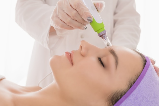 A young beautiful woman in the cosmetologists office receives fractional mesotherapy for her face.