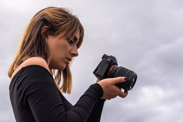 Young beautiful woman in dark sweater looking down at mirrorless camera display