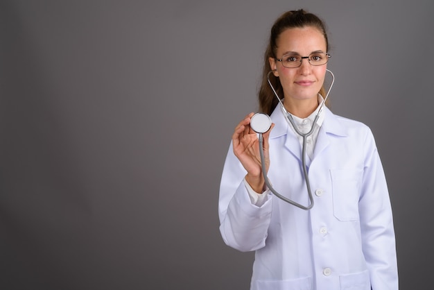 Young beautiful woman doctor against gray background