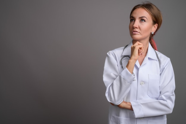 Young beautiful woman doctor against gray wall