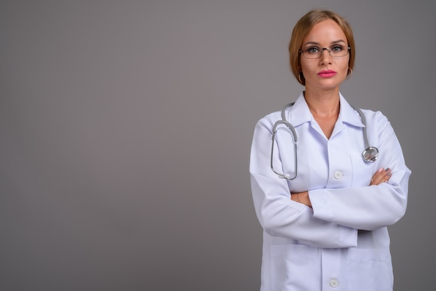 Young beautiful woman doctor with blond hair against gray backgr