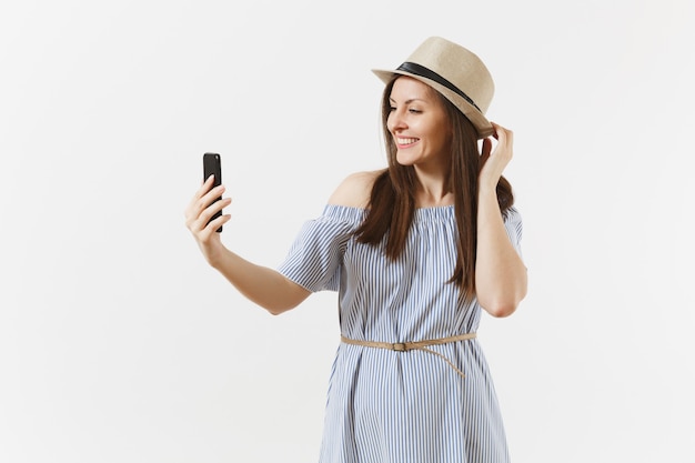 Young beautiful woman dressed blue dress, hat doing selfie shot on mobile phone or video call isolated on white background. People, sincere emotions, lifestyle concept. Advertising area. Copy space.