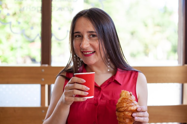 Young beautiful woman eating croissant and drinking coffee