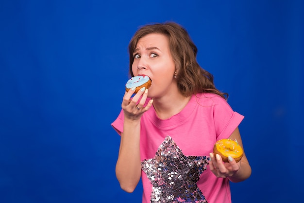 Young beautiful woman eating doughnuts on blue.