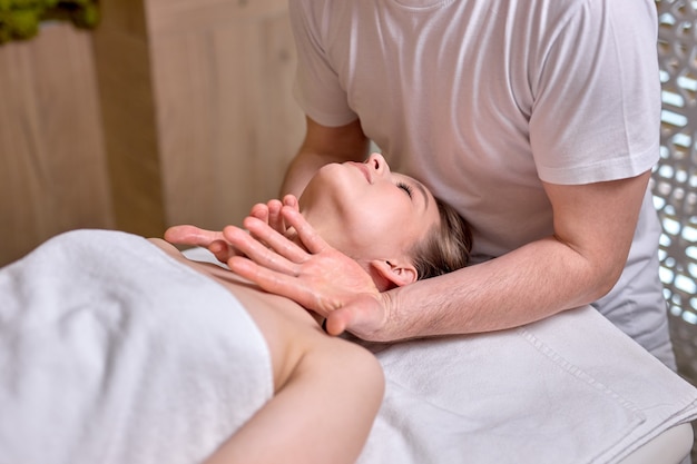 Young beautiful woman enjoying facial massagemale therapist making head and neck massage to female client