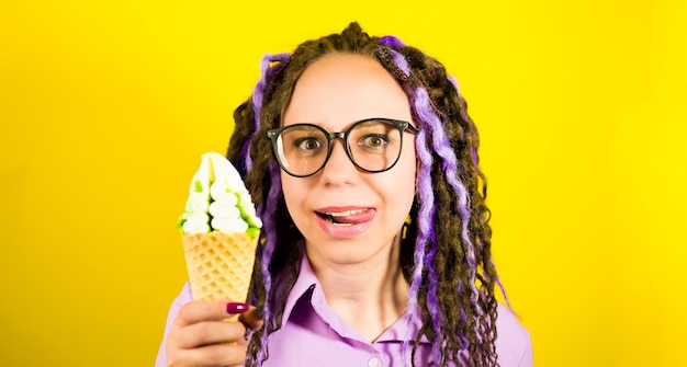 Young beautiful woman in glasses licking lips on yellow background Portrait of happy female with dreadlocks in anticipation enjoying sundae