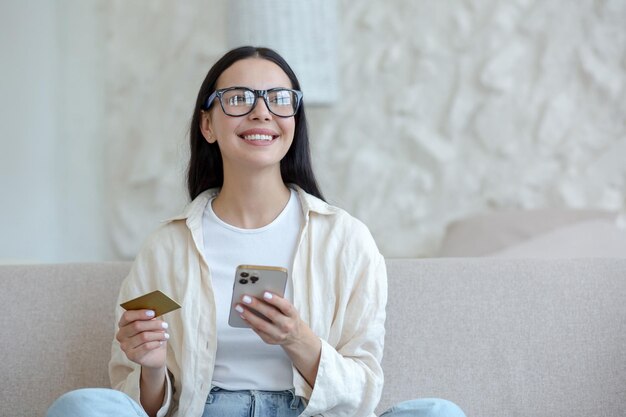 Young beautiful woman in glasses smiling and happy doing online shopping in online store sitting on