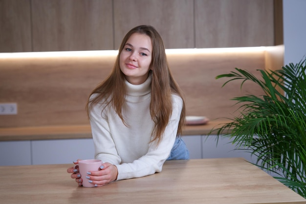 Young beautiful woman happy girl standing at home at kitchen drinking tea or coffee from cup smile