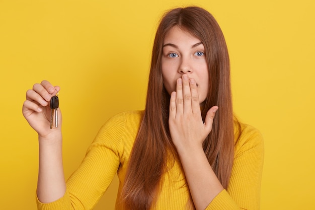 Young beautiful woman holding home key on yellow