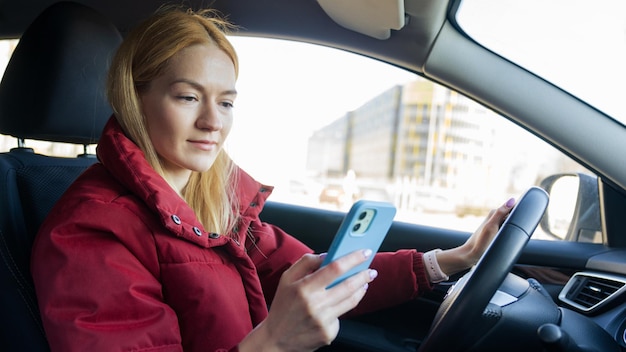 A young beautiful woman is driving a car and typing on her phone