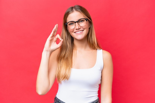 Young beautiful woman isolated on red background showing ok sign with fingers