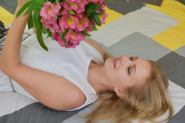 young beautiful woman lies on bed with a bouquet of fresh flowers