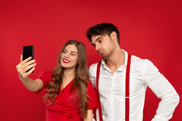 Young beautiful woman and man embrace in elegant outfits taking selfie