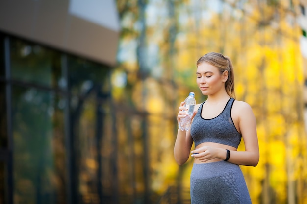 Young beautiful woman in the park wearing sportwear and drinking water