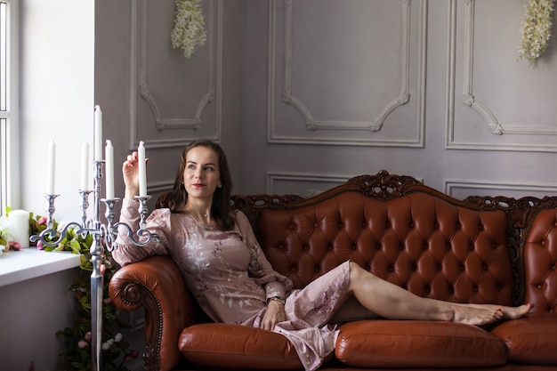 Young beautiful woman in pink dress sits on brown leather sofa