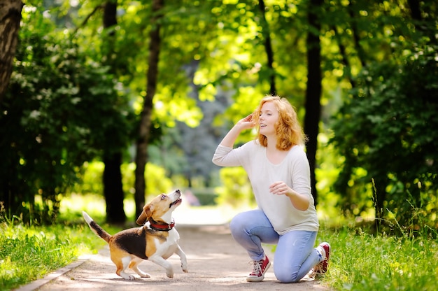 Young beautiful woman playing with Beagle dog in the summer park