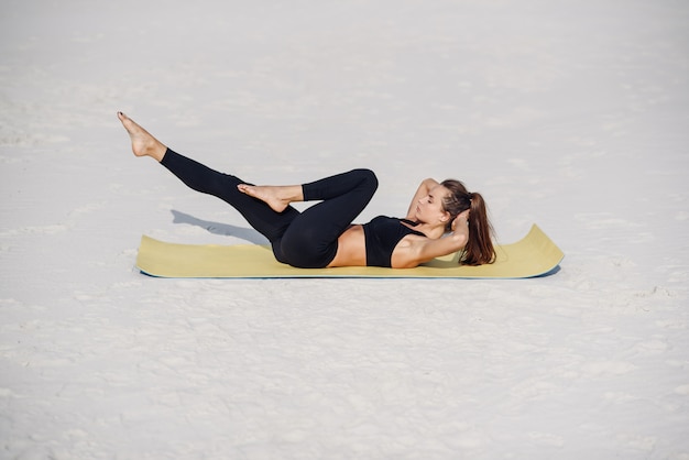 Young beautiful woman practicing yoga, doing press ups exercise on the beach of the sea. Fitness yoga and healthy lifestyle concept. Beautiful woman in sports wear doing exercise on yoga mat.