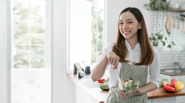 Young beautiful woman prepares cooking healthy food from fresh vegetables and fruits in kitchen room Smiling and looking at camera