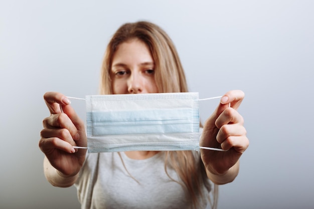 Young beautiful woman put on medical mask for protection against coronavirus contagious disease on a light background Medic holding face mask Preventive measure against coronavirus COVID19