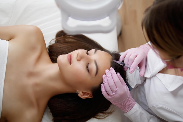 Young beautiful woman receiving hair mesotherapy injections from a professional trichologist