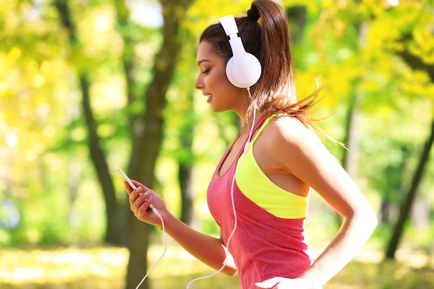 Young beautiful woman running in autumn park and listening to music with headphones